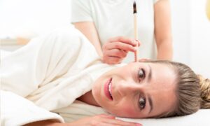 A woman lying on her side and a hand beside her (therapist) performing ear candling treatment.