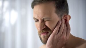 Man holding his aching ear, suffering from otitis diseases, sudden hearing loss, close up