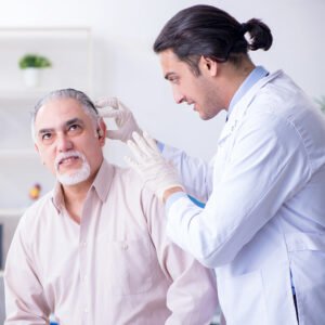 Doctor adjusting hearing aid on middle-aged male patient