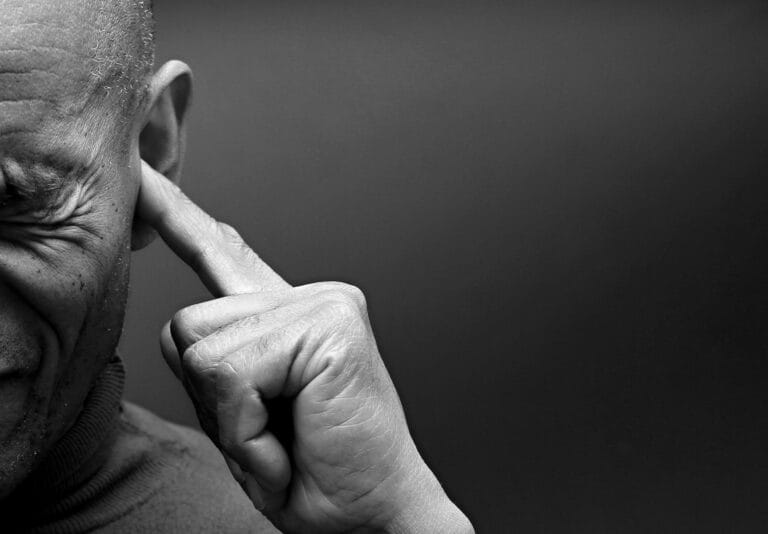 Old man pressing hsi ears with index finger experiencing ear discomfort and potential tinnitus caused by chronic stress.