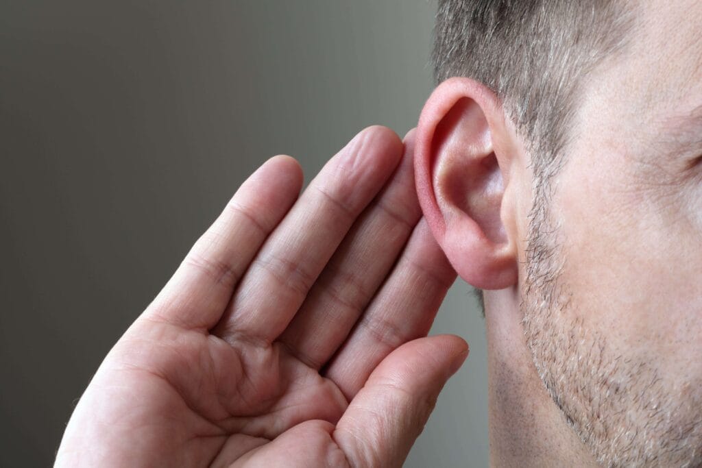 Closeup of a man with his hands near his ear trying to listen.