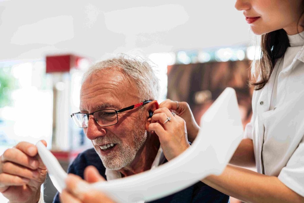 Nurse helping elderly man wear hearing aid.