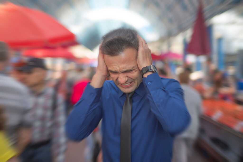 a man with his hands to his ears and his surrounding is blurred.